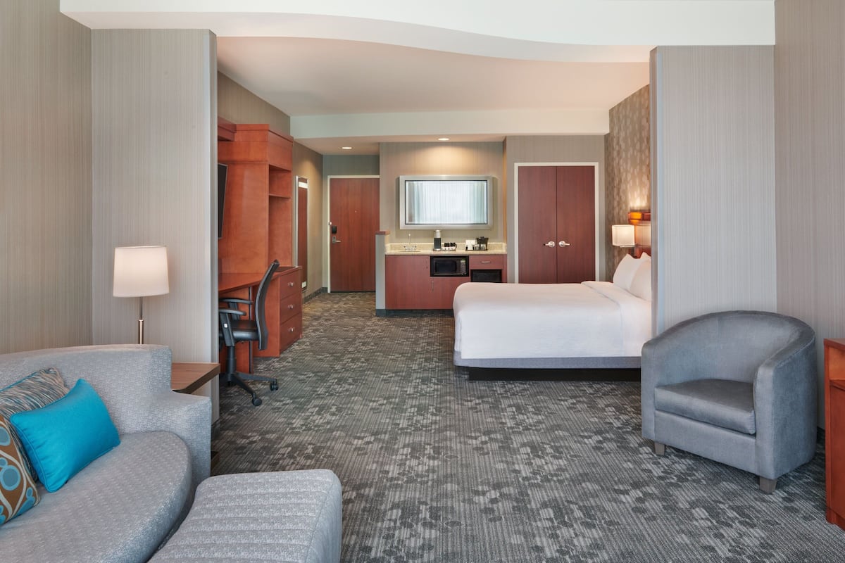 A hotel room with a bed, a desk with a microwave, a chair, a sofa, and a lamp.