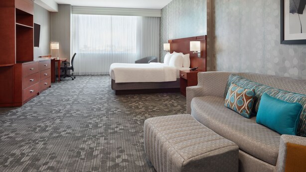 A hotel room with a bed, a sofa, a desk, and a wardrobe. - Courtyard by Marriott Ottawa East (Ottawa)