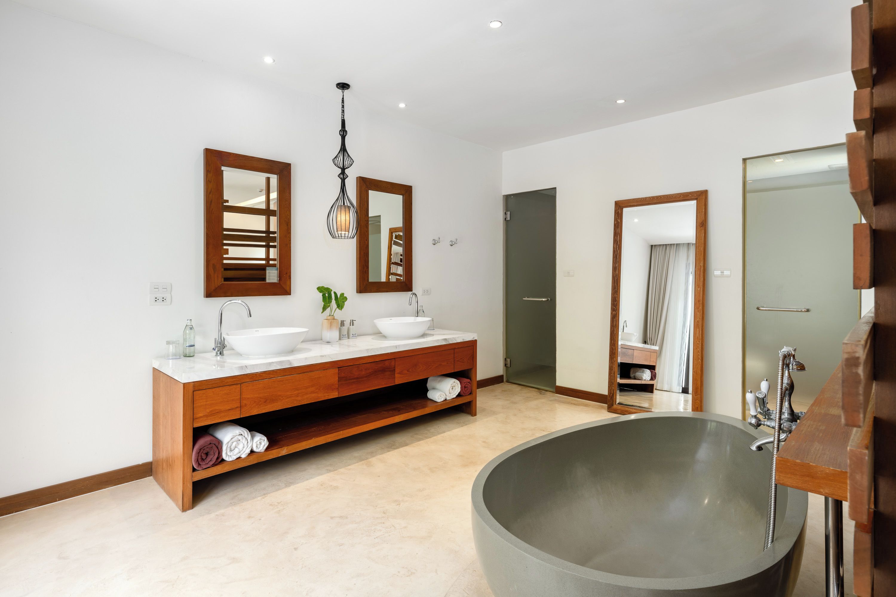 Un bagno moderno con una grande vasca da bagno freestanding, un mobile bagno in legno con due lavandini e uno specchio grande sopra il mobile.