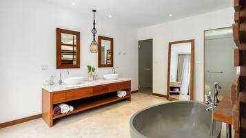 Un bagno moderno con una grande vasca da bagno freestanding, un mobile bagno in legno con due lavandini e uno specchio grande sopra il mobile.