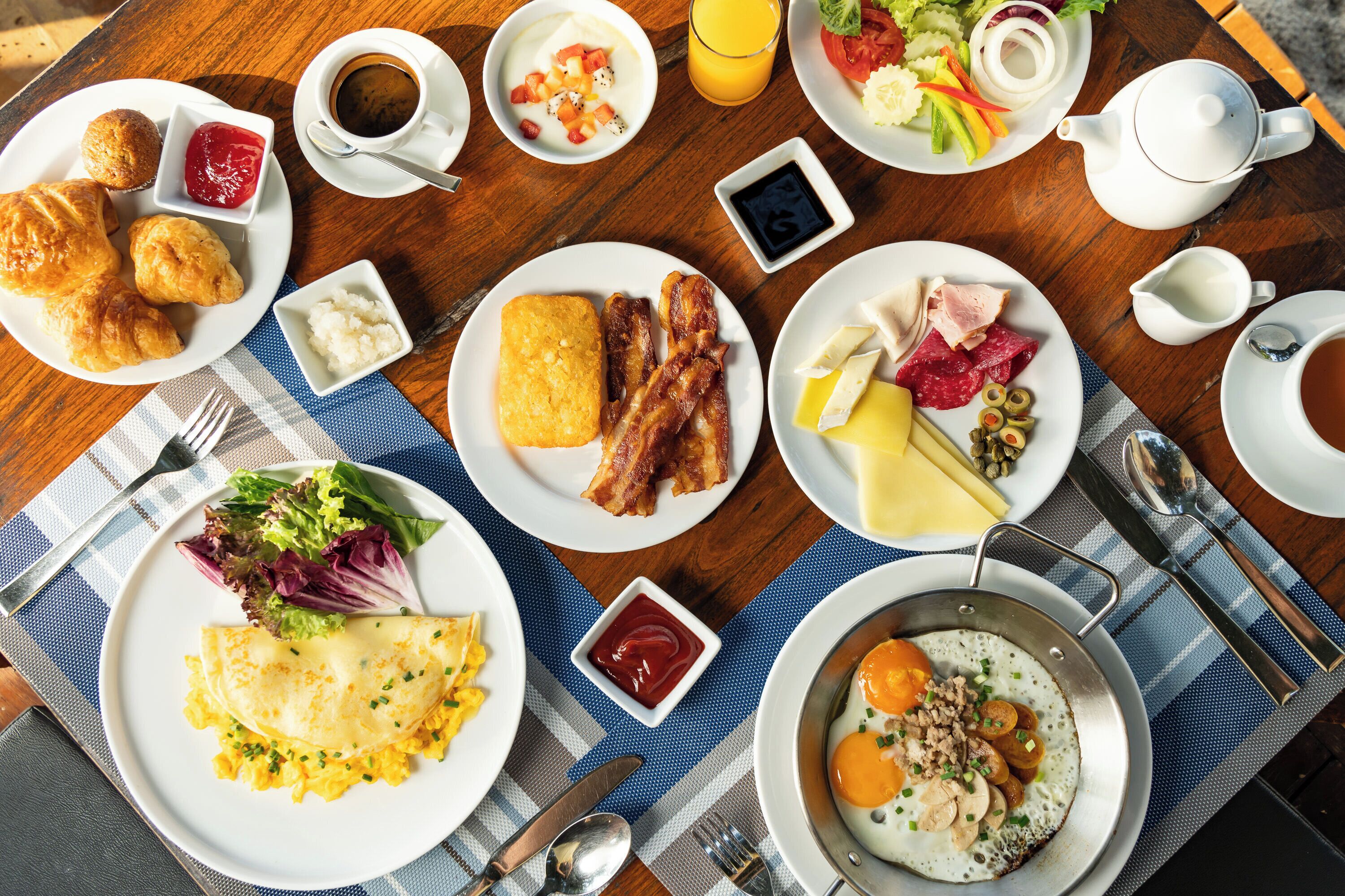 A breakfast table with various dishes including eggs, bacon, toast, and a fruit salad.