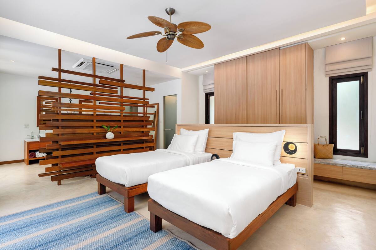 A modern hotel room with two beds, a ceiling fan, wooden headboard, and a large window.