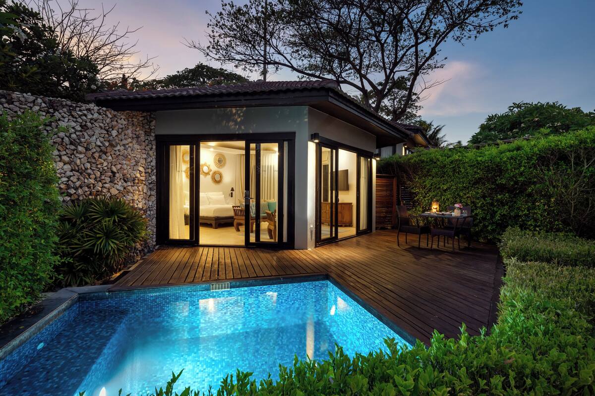 A modern house with a swimming pool, wooden deck, and a stone wall.