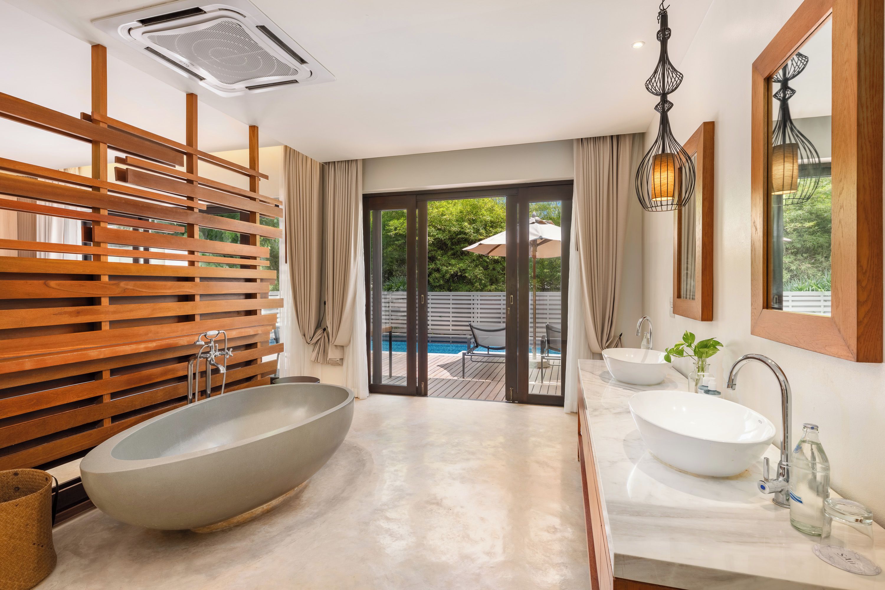 A modern bathroom with a large freestanding bathtub, a double sink vanity, and a view of an outdoor pool area.