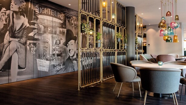 Un interior moderno con un gran mural en la pared, una mesa redonda con sillas y un separador metálico decorativo.