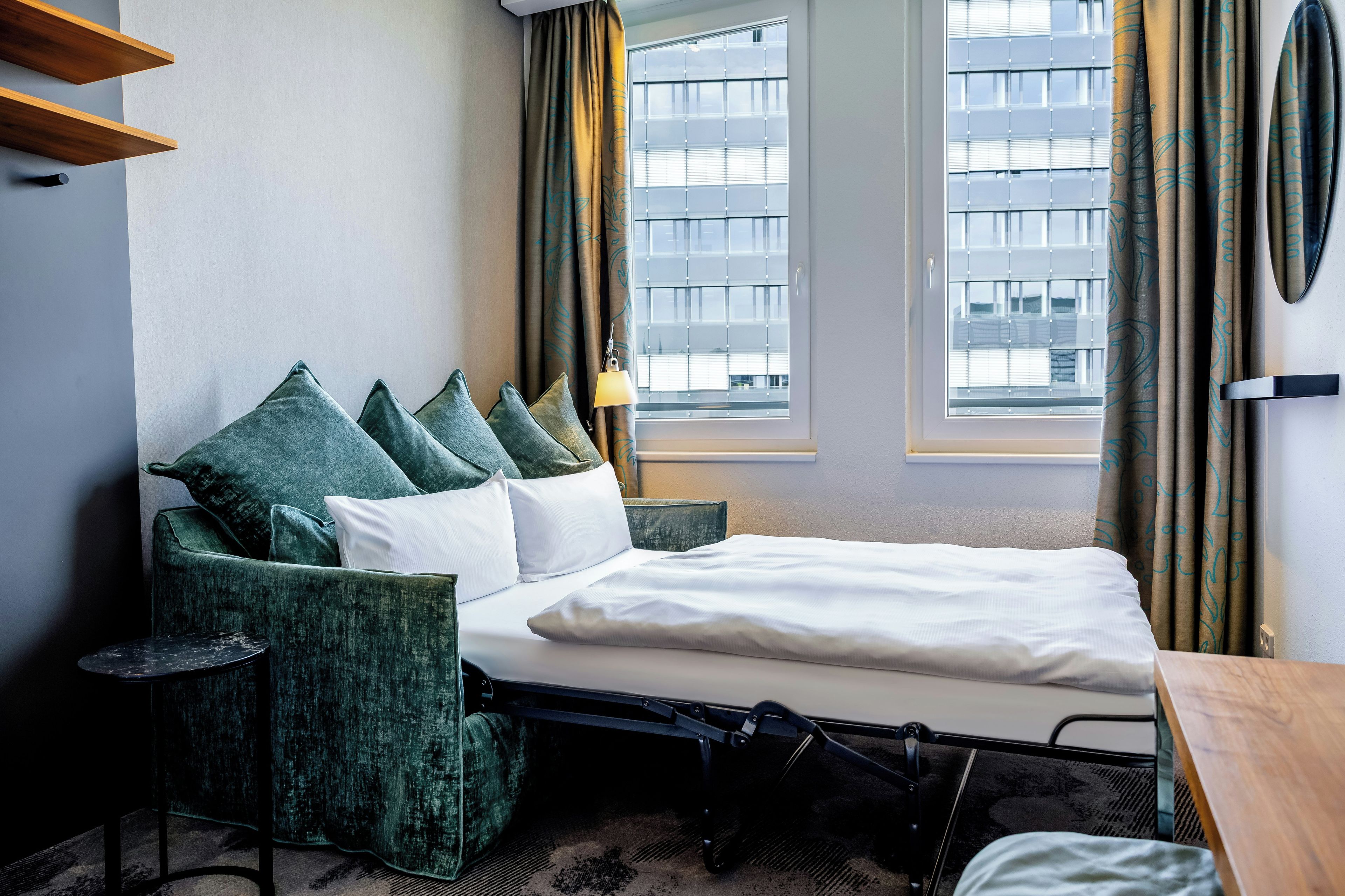 Une chambre d’hôtel avec un lit, une chaise, une lampe et une fenêtre avec des rideaux.