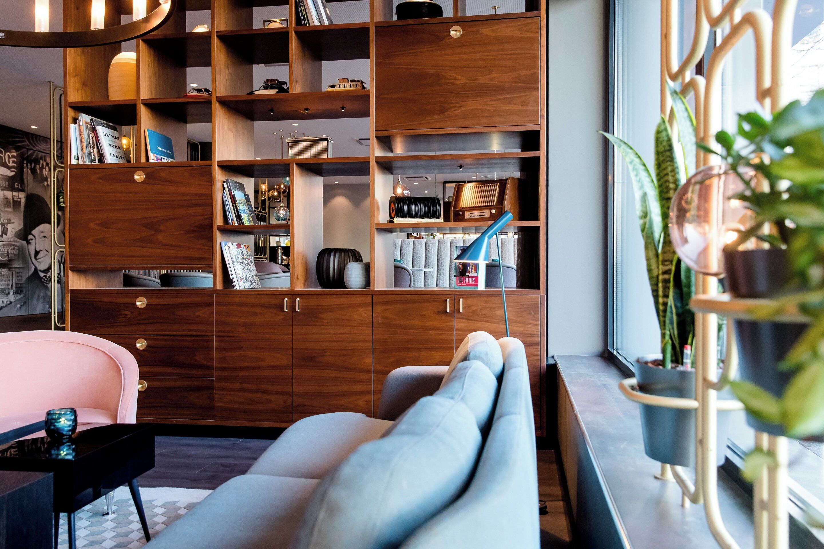 Ein modernes Wohnzimmer mit einem großen Bücherregal aus Holz, einer bequemen Couch und einem Topf mit Pflanze.