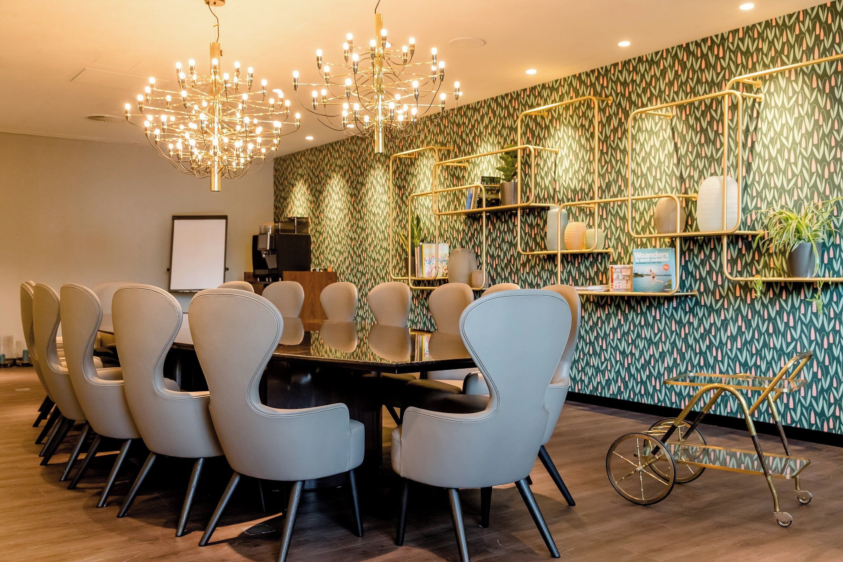 A conference room with a round table, modern chairs, a chandelier, patterned wallpaper, and a metal cart.