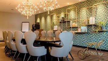 A conference room with a round table, modern chairs, a chandelier, patterned wallpaper, and a metal cart.