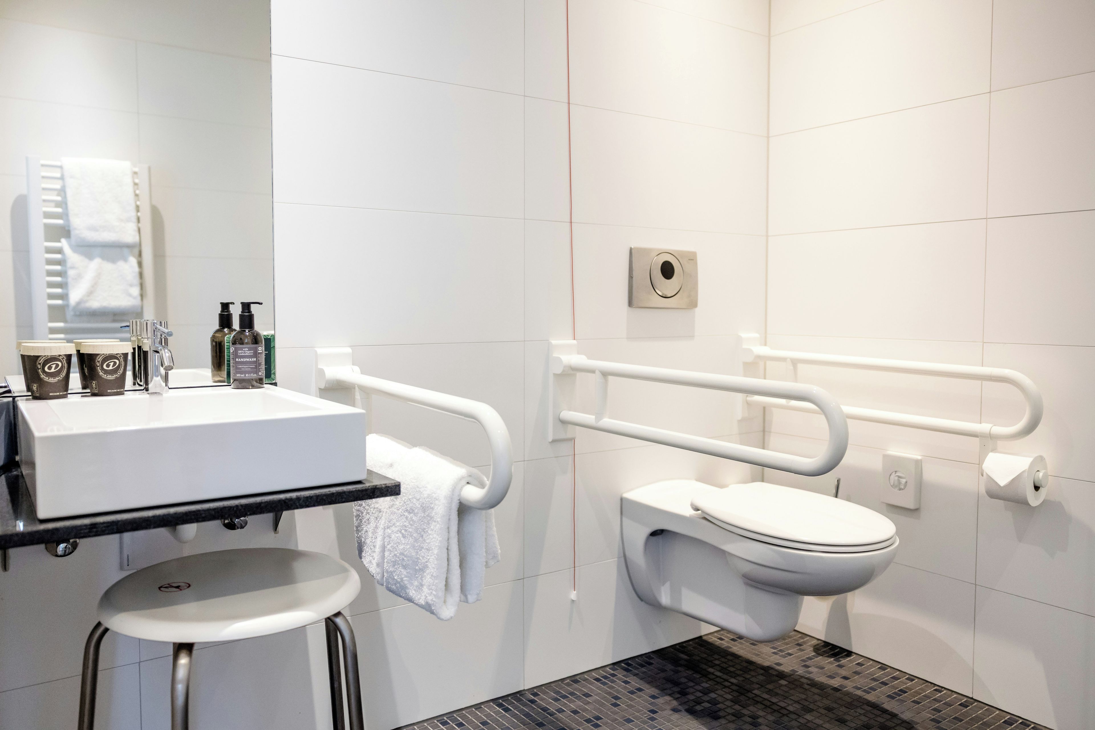 Une salle de bain moderne avec un lavabo, des toilettes et une barre d’appui, le tout de couleur blanche.