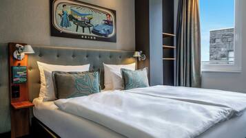 A hotel room with a bed, a wall-mounted artwork, a nightstand, a lamp, and a window with curtains.