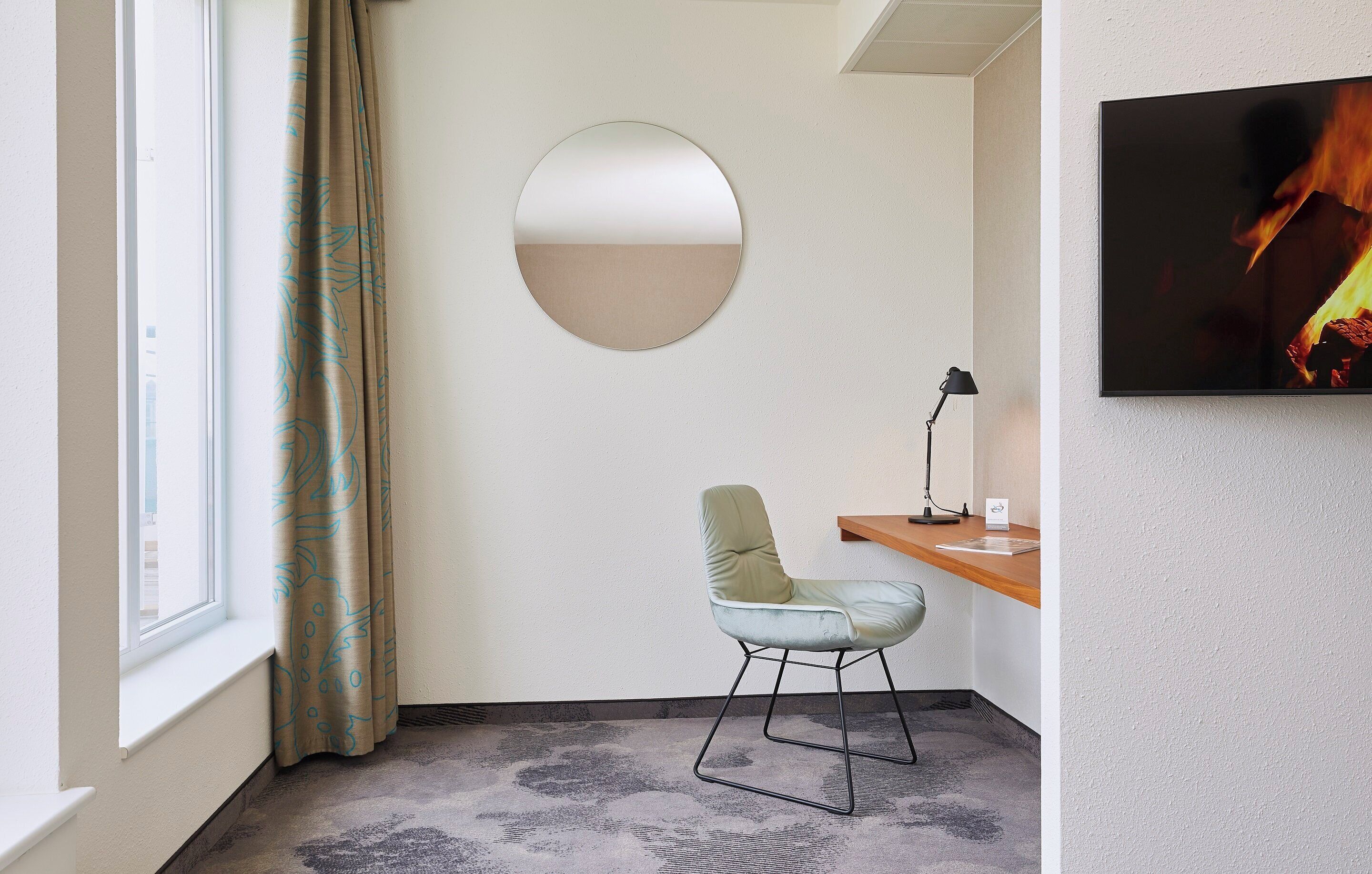 A modern room with a round mirror, a desk with a lamp, and a television.