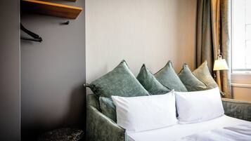 Quarto de hotel com cama, almofadas, abajur e janela com cortinas.