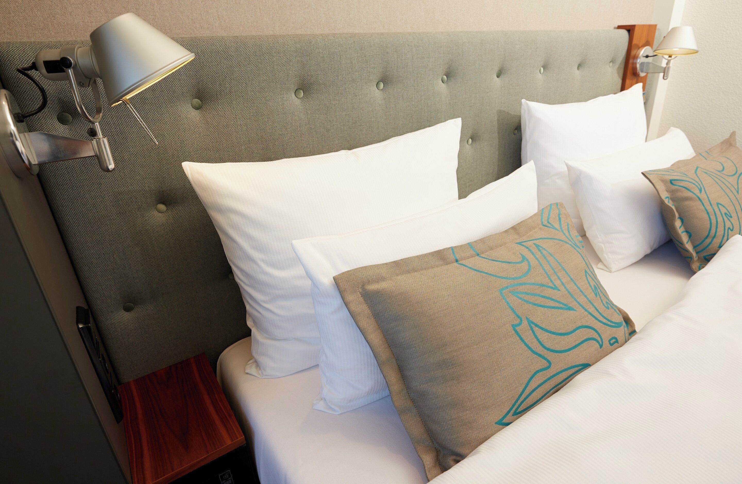 A hotel room with a tufted headboard, white bedding, and decorative pillows.