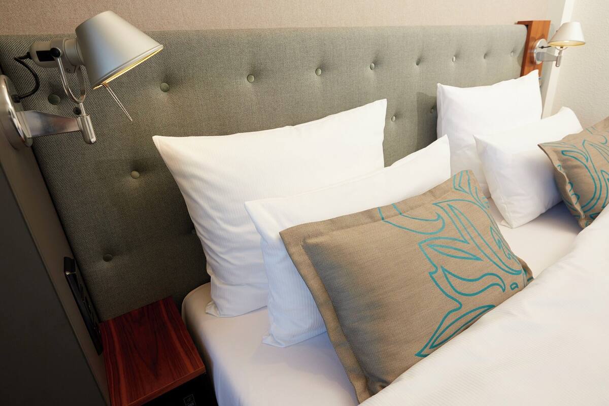 A neatly made bed with white and patterned pillows, a tufted headboard, and bedside lamps.