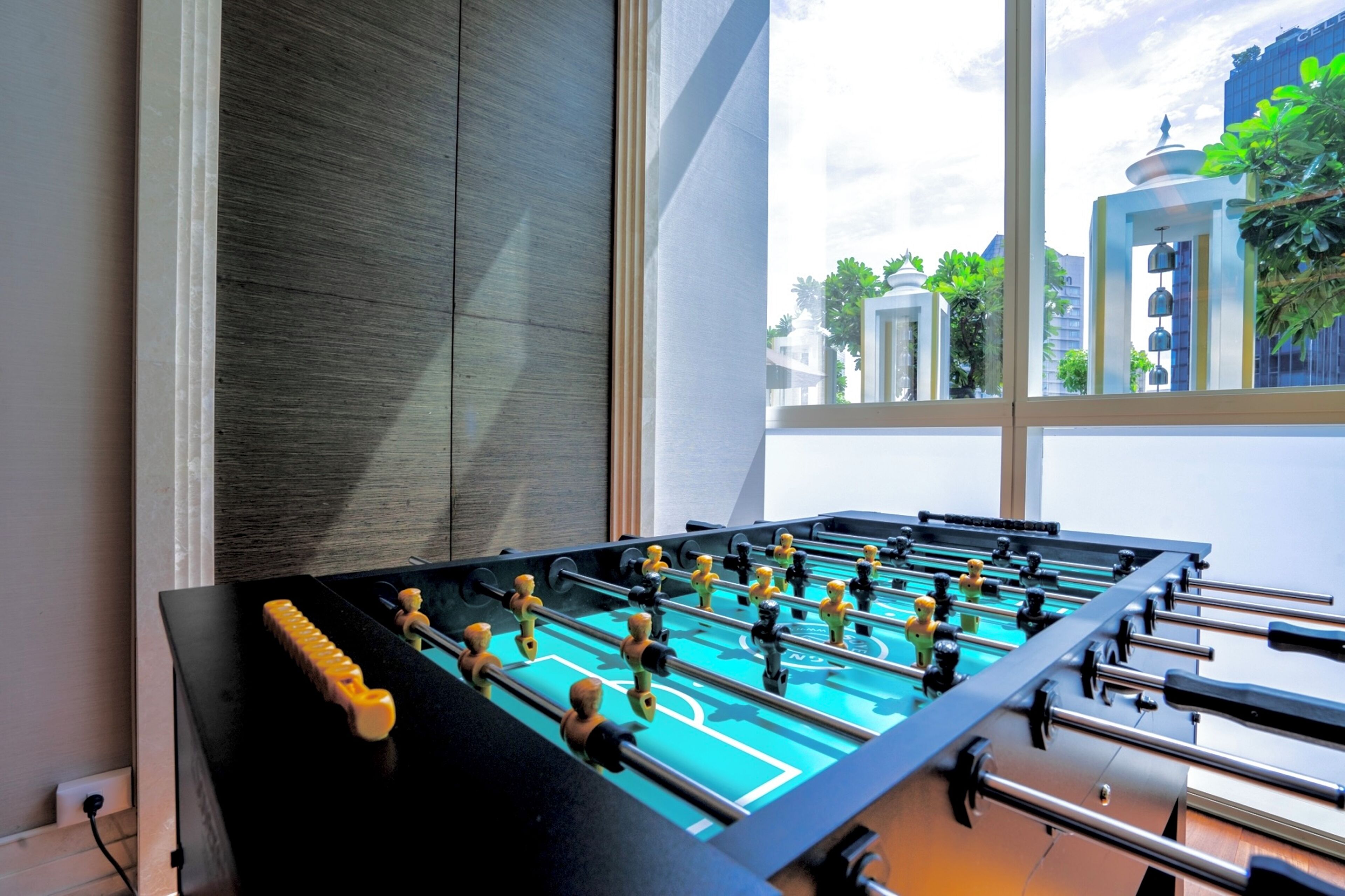 A foosball table in a room with large windows, offering a view of buildings and greenery outside.
