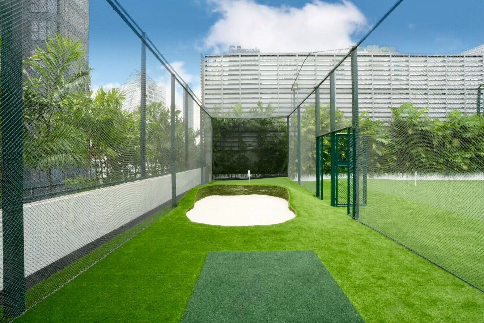 A golf practice area with a sand trap, surrounded by green artificial turf and enclosed by a netted fence.