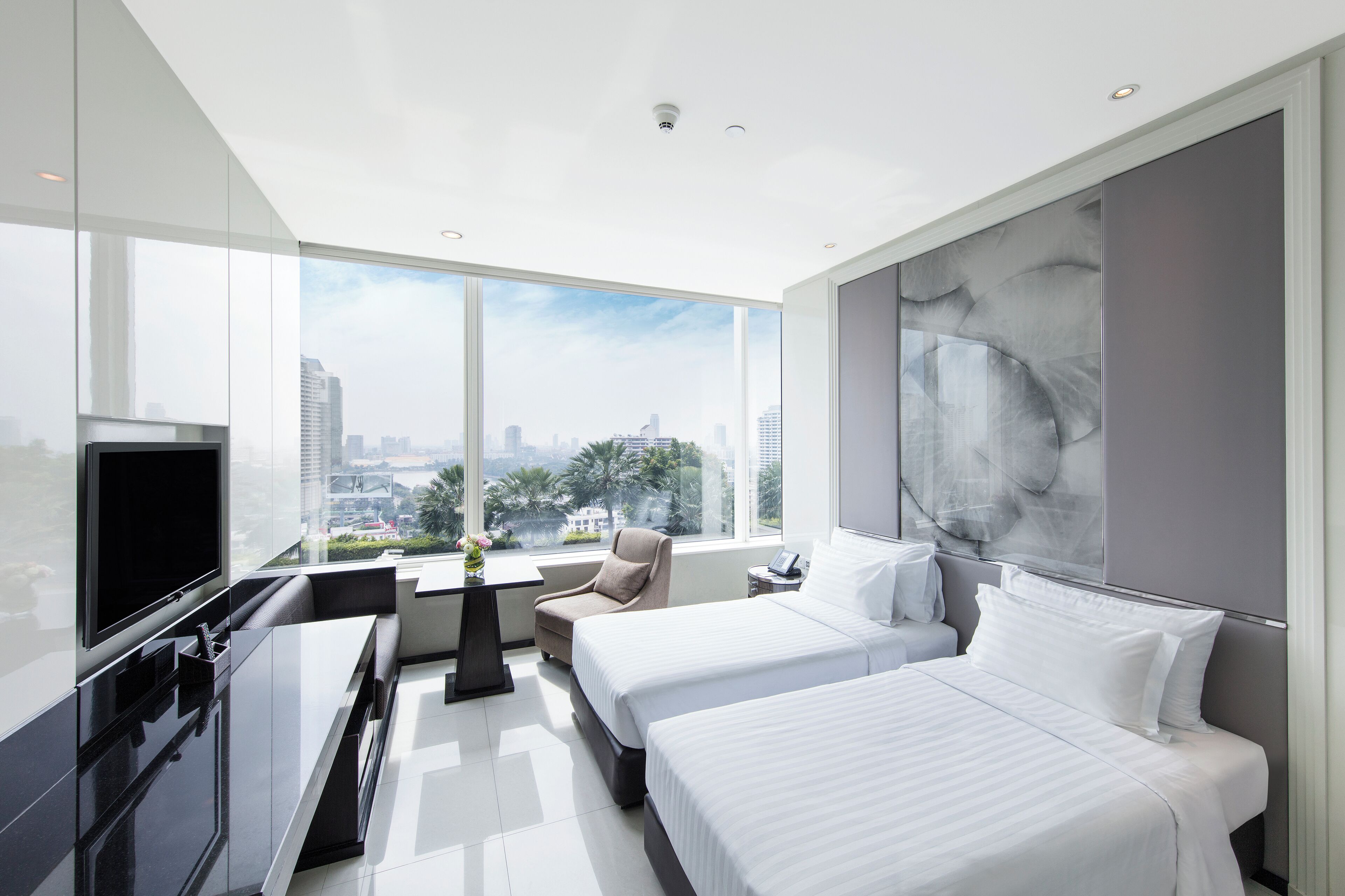 A modern hotel room with a large window, a flat-screen TV, two beds, a desk, and a chair.