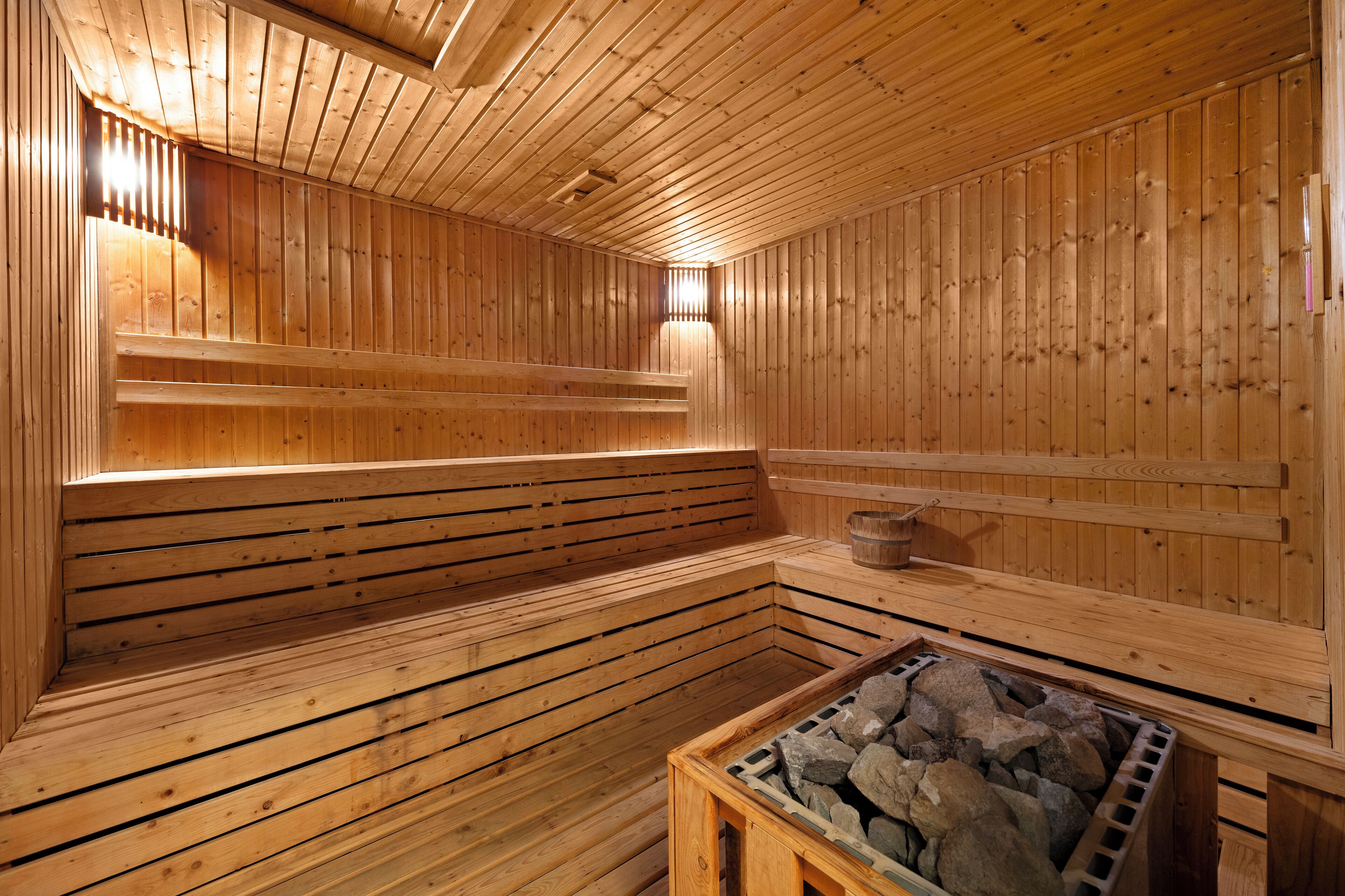 A sauna with wooden walls and benches, a stone heating element, and a wooden bench in the foreground.