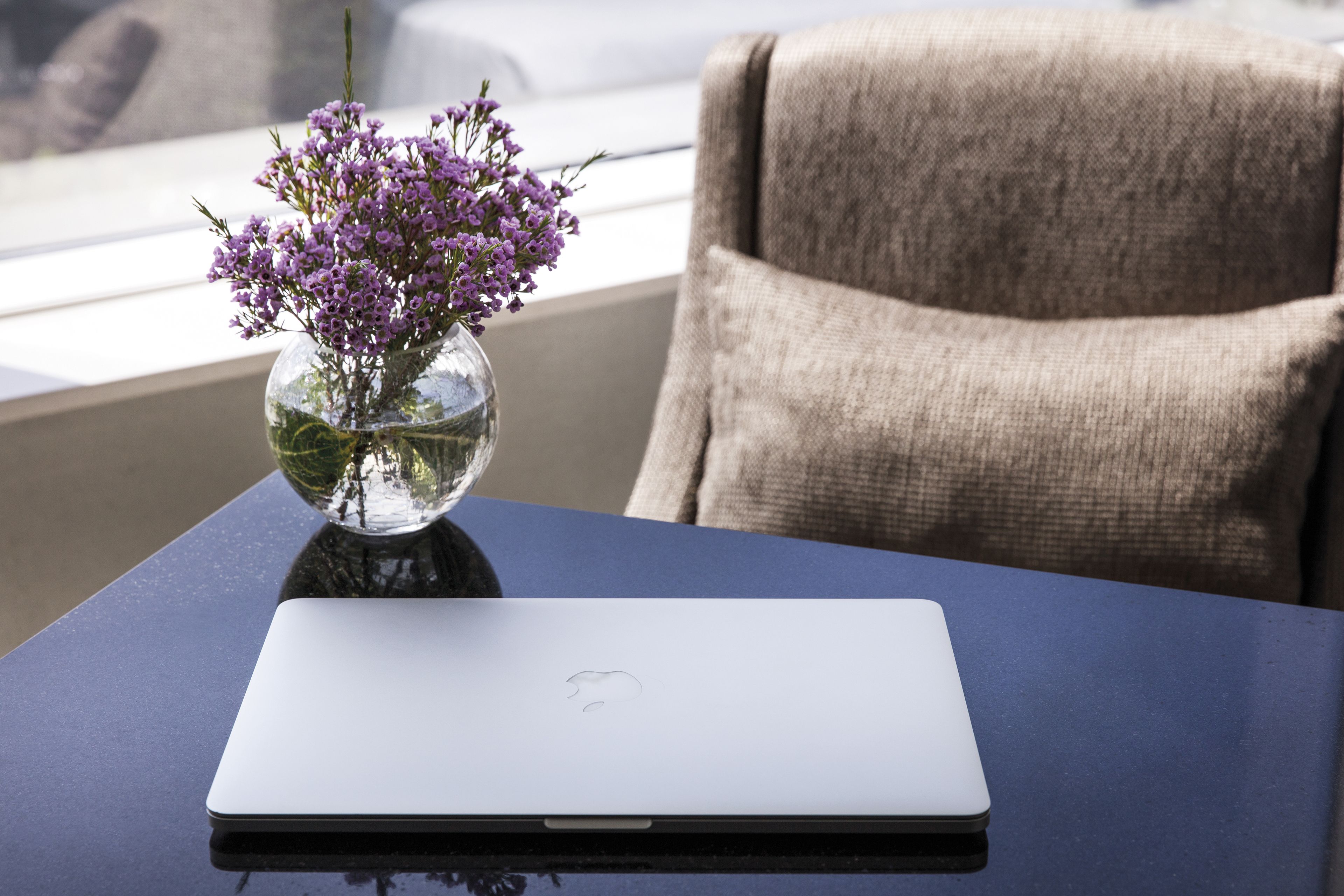 A laptop on a table with a vase of purple flowers.