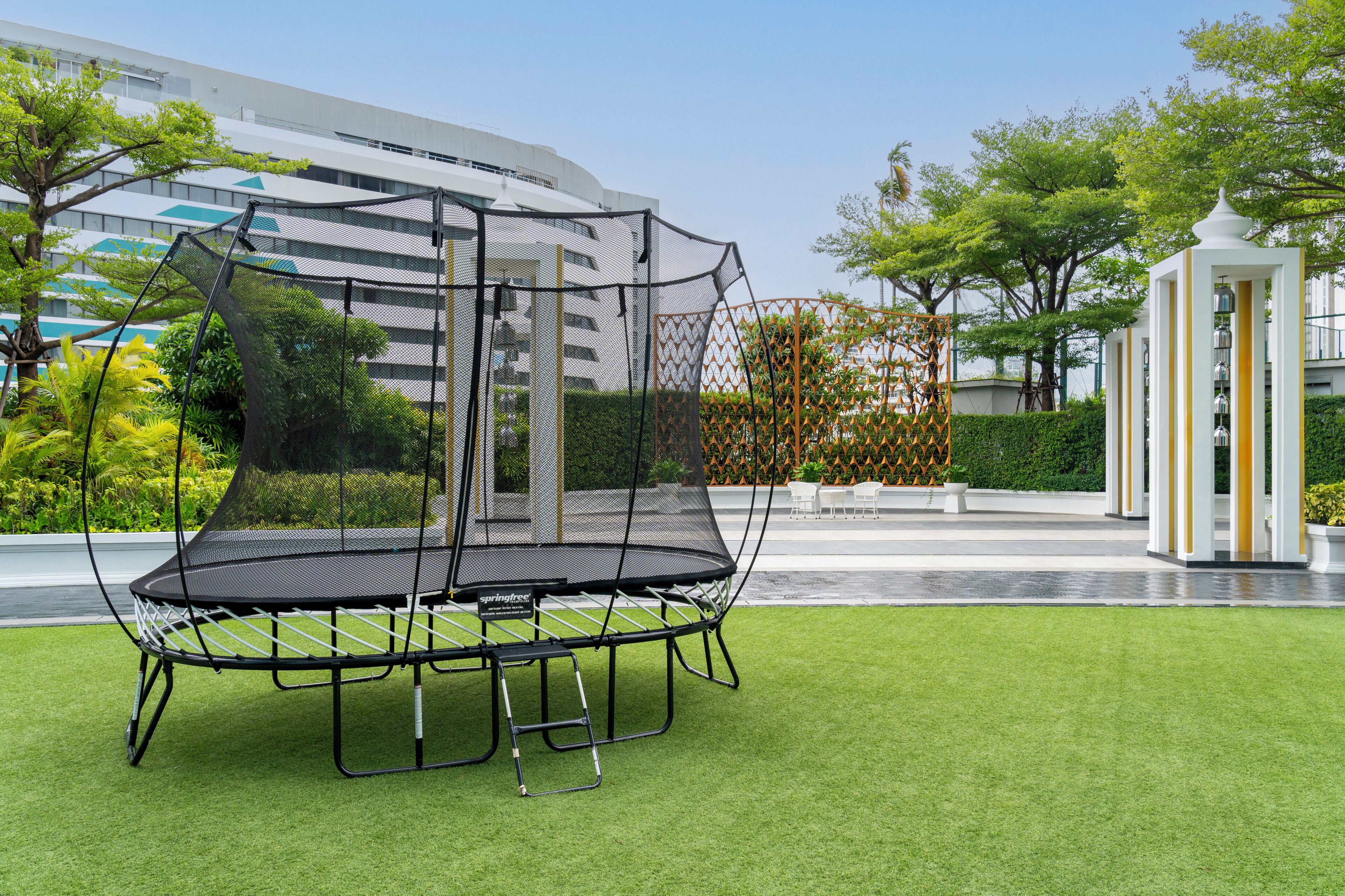 A trampoline in a landscaped area with a building in the background.