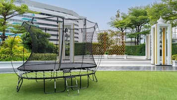 A trampoline in a landscaped area with a building in the background.