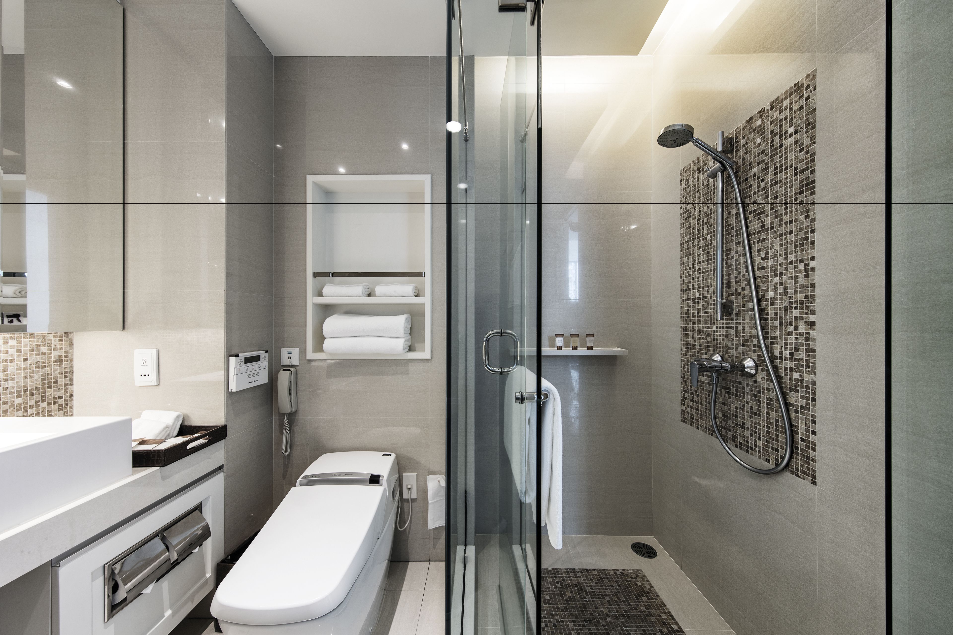 A modern bathroom with a glass-enclosed shower, a toilet, a vanity with a mirror, and a shelf with towels.