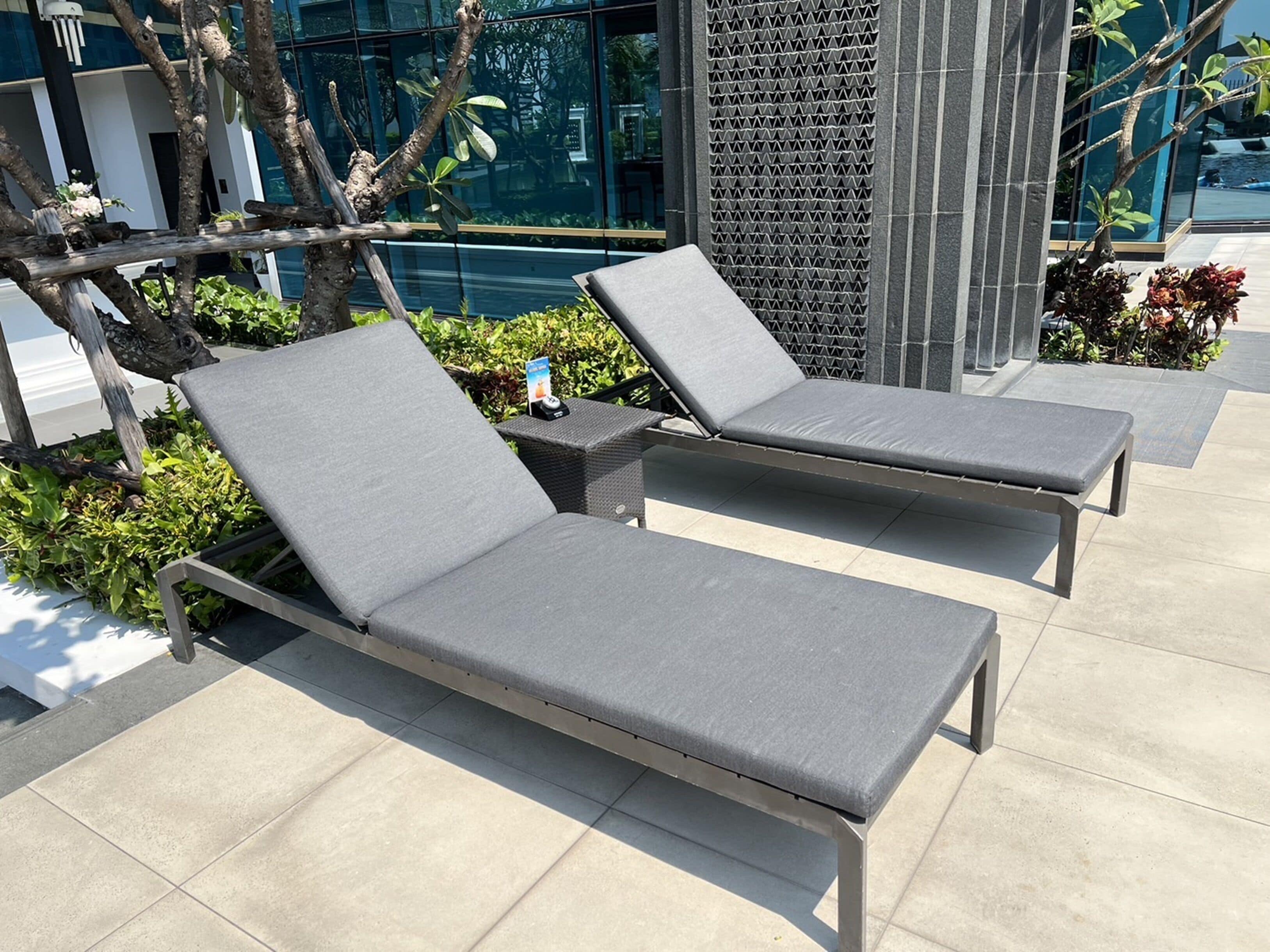Two lounge chairs with grey cushions, a small table with a bottle, and a decorative wall with a geometric pattern.