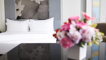 A hotel room with a bed, white pillows, a floral wall decoration, and a vase with flowers.