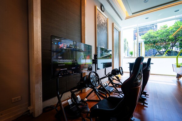 A modern room with a large flat-screen TV mounted on the wall, a gaming chair, and a desk with a computer.