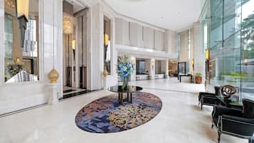 A spacious lobby with a central round table, seating area, and a large glass wall providing a view of the outdoors.