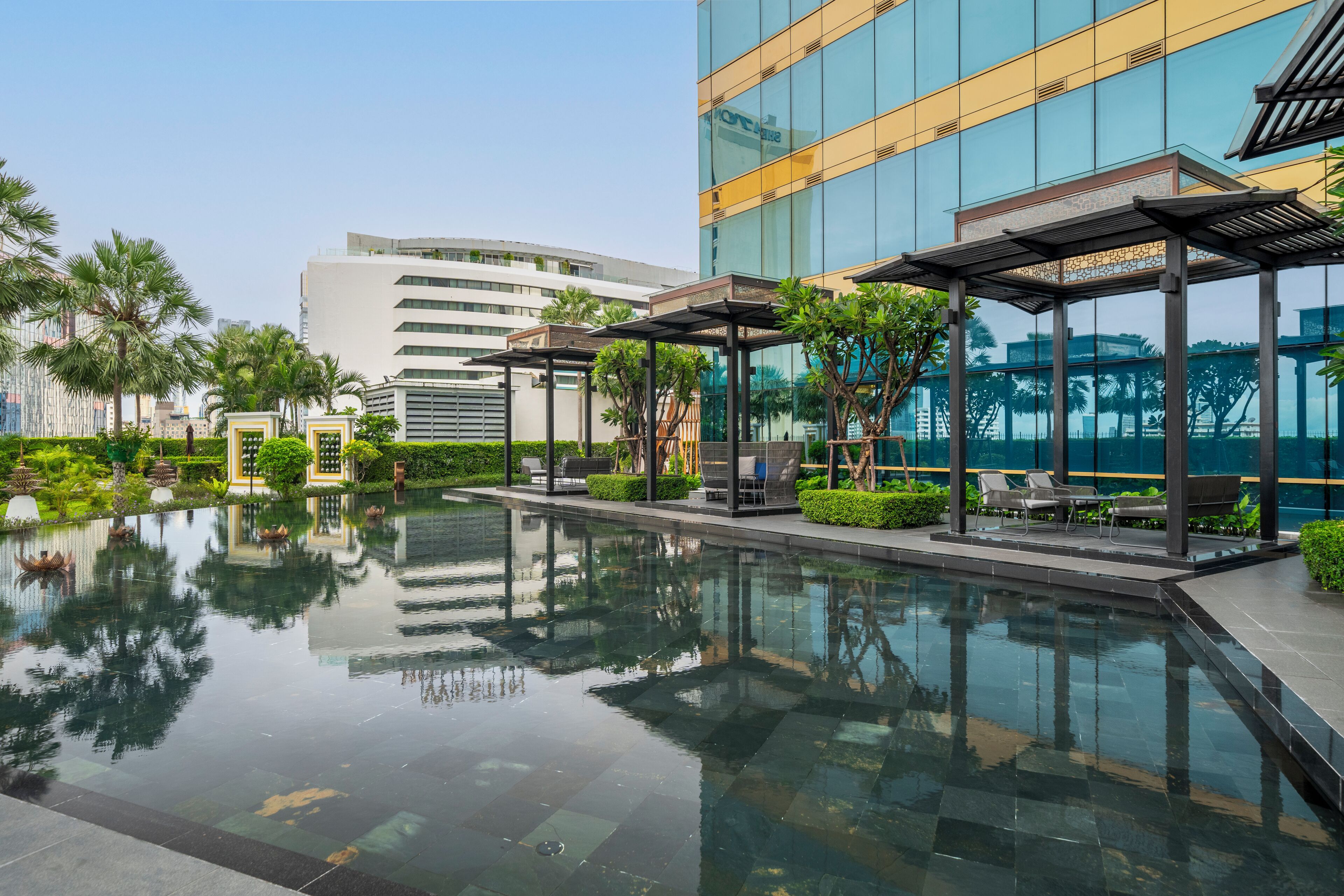 A modern hotel with a reflective pool, outdoor seating, and lush landscaping.