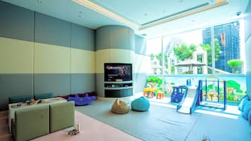 A modern living room with a flat-screen TV, seating, and a play area with a slide and climbing structure.