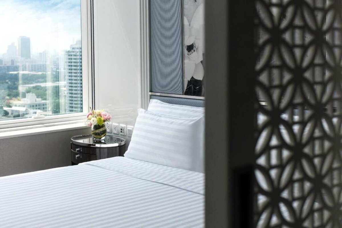 A hotel room with a bed, a small table with a vase of flowers, and a view of the city through a window.