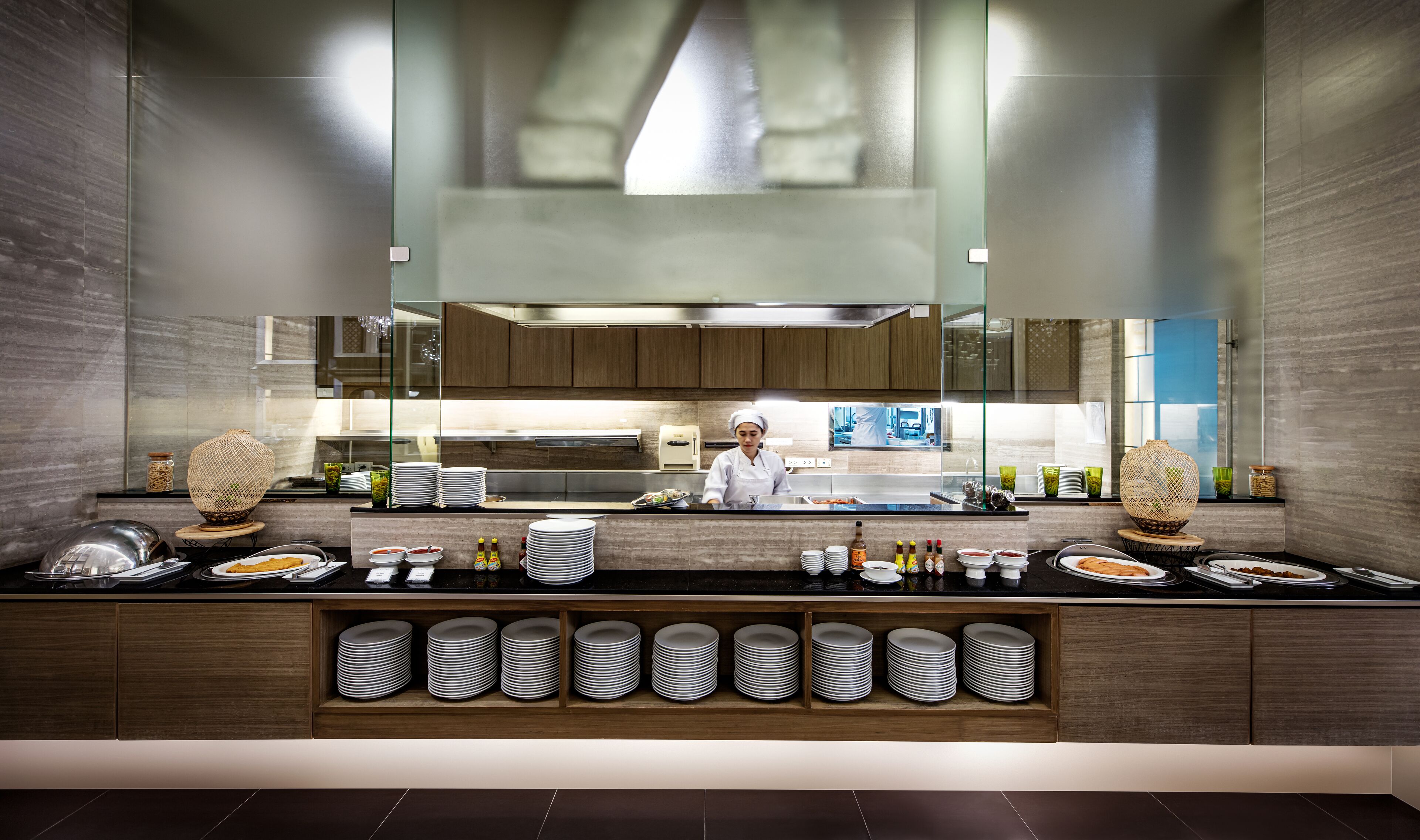 A modern kitchen with a chef preparing food, wooden cabinets, and a large mirror above the counter.