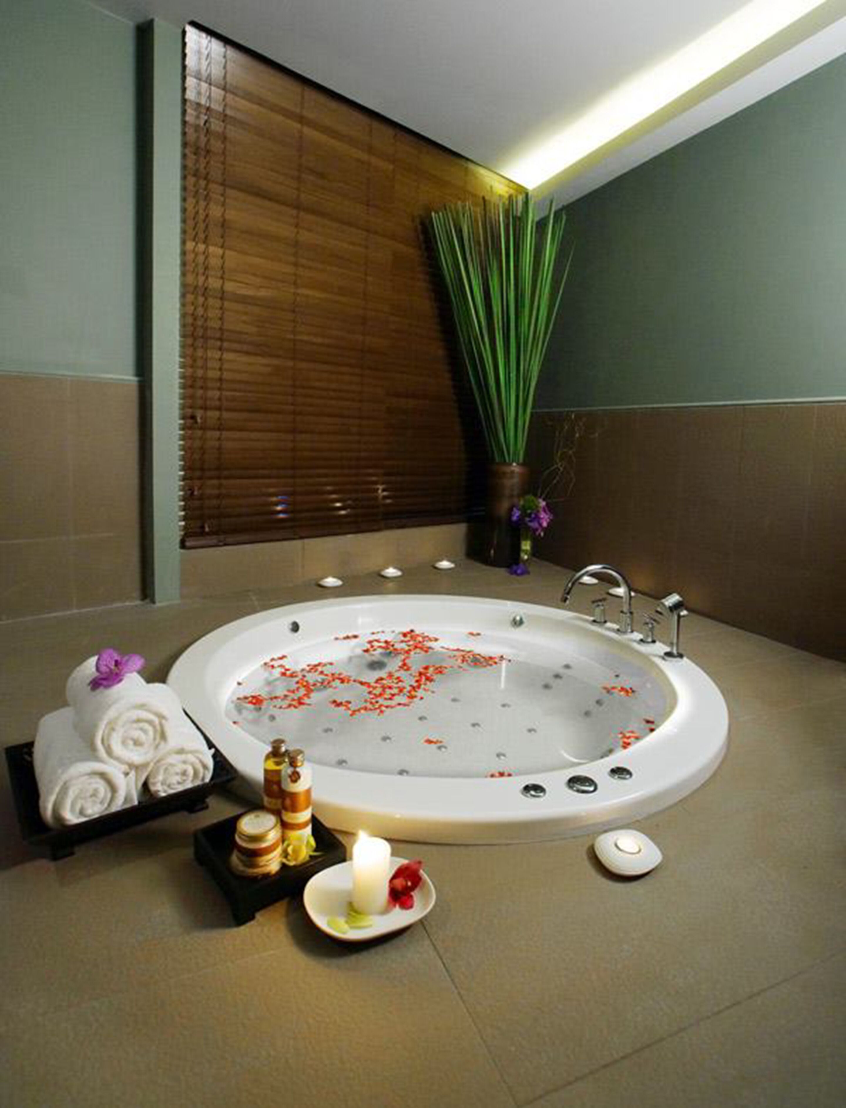 A bathroom with a large bathtub, a wooden blind, a potted plant, and toiletries on the counter.