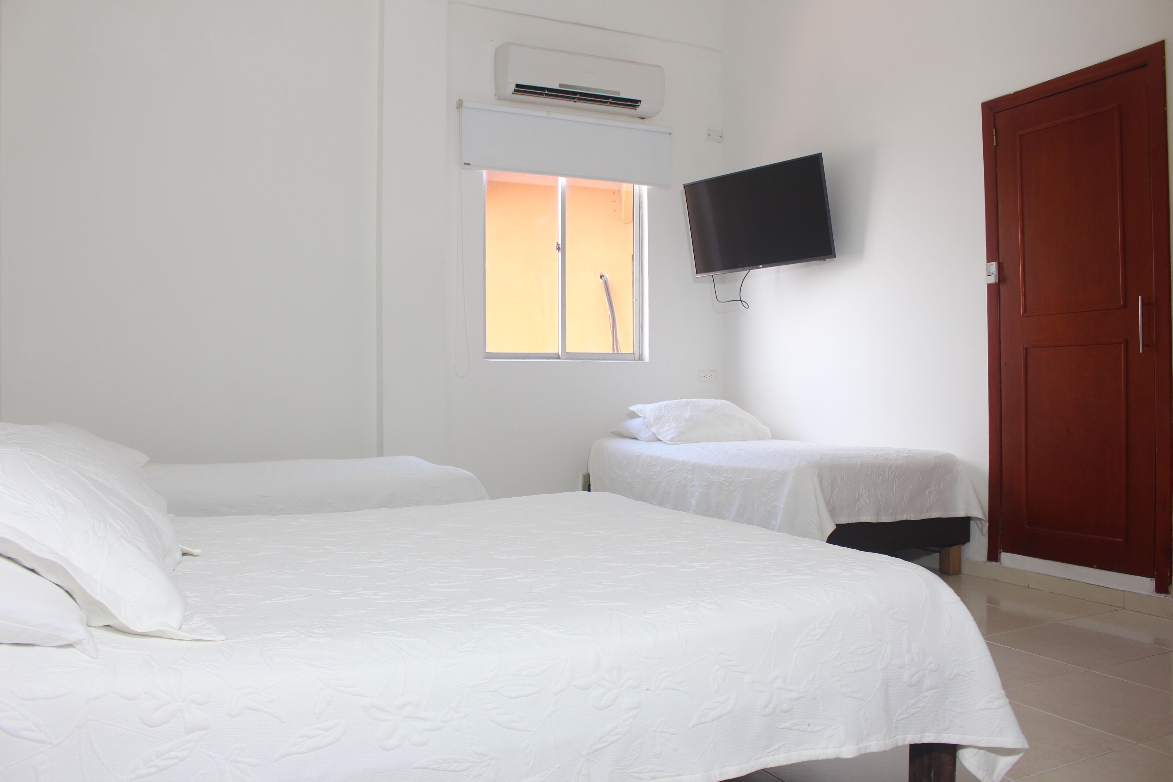 A hotel room with two beds, a TV mounted on the wall, and a window with a view.