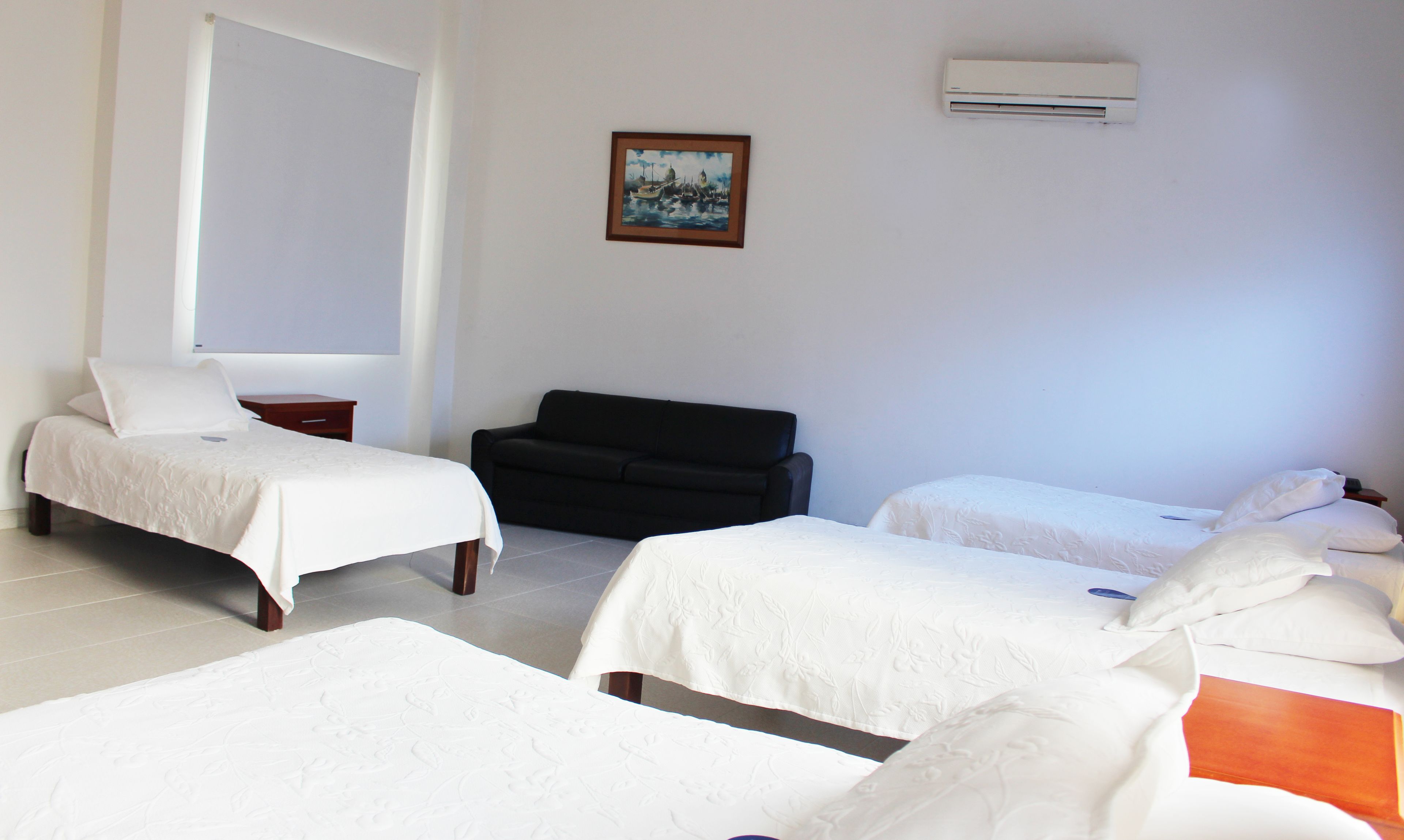 A hotel room with two single beds, a sofa, a small table, and a painting on the wall.