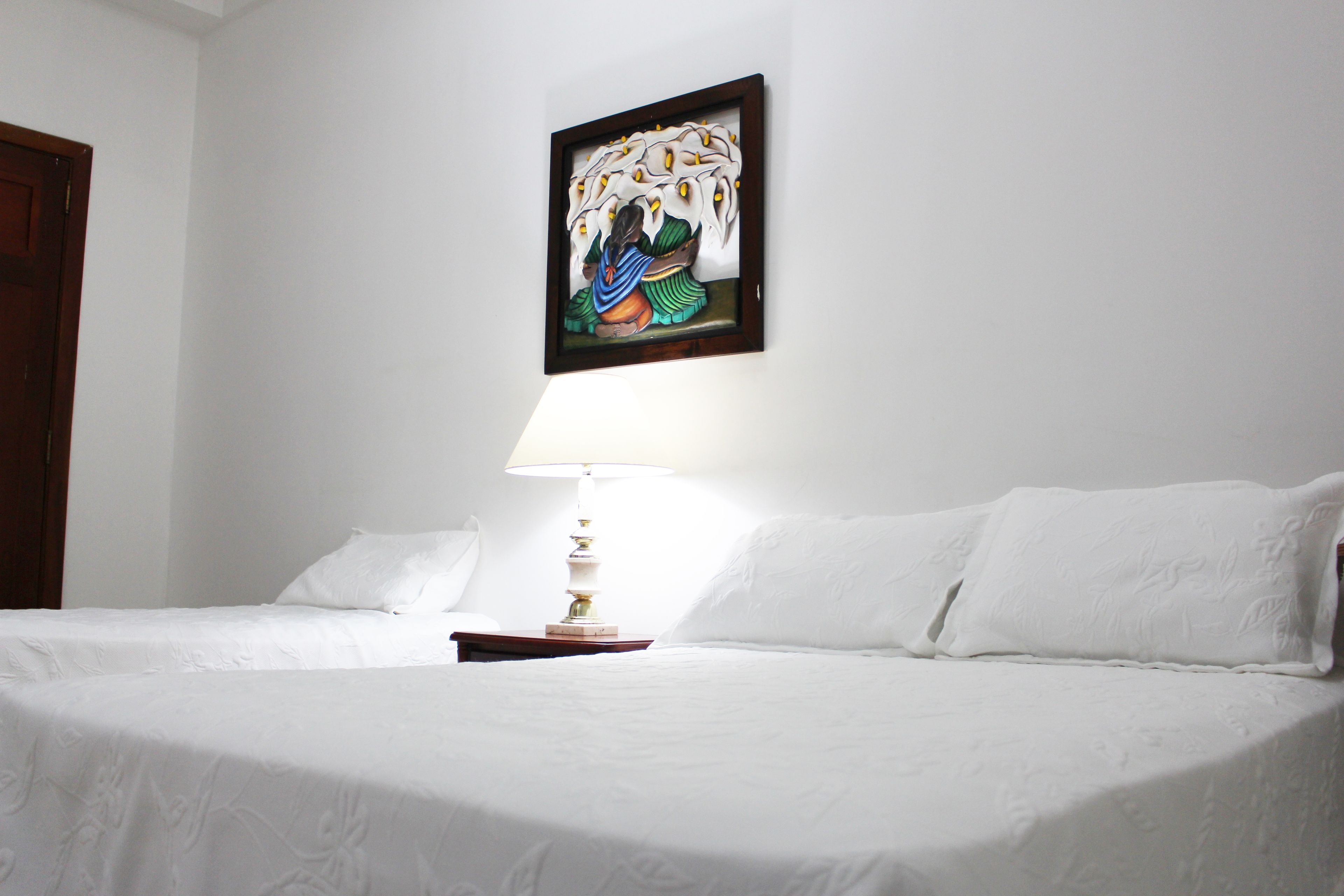 Una cama bien tendida con sábanas blancas y una mesita de noche con una lámpara.