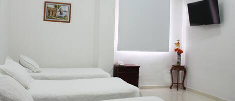 Habitación de hotel con dos camas, una mesita de noche pequeña con un teléfono, televisión montada en la pared, un cuadro enmarcado y una ventana con persianas.