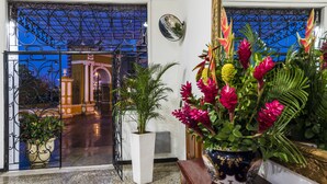 Entrada de hotel con una reja de hierro forjado, plantas en macetas y vista del interior.
