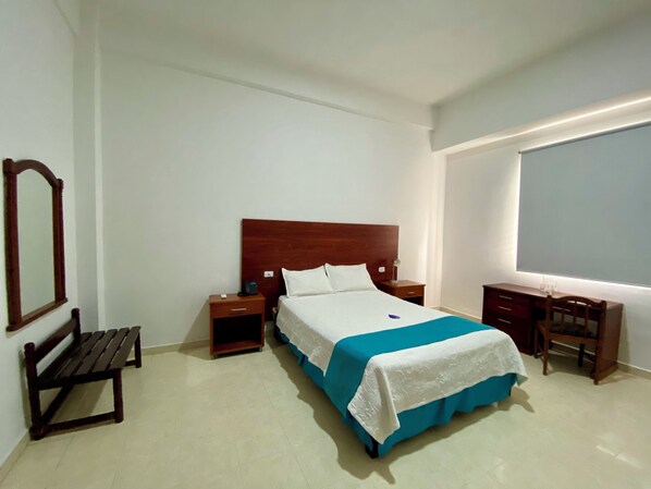 Una habitación de hotel con cama, mesita de noche, escritorio, silla y banca.