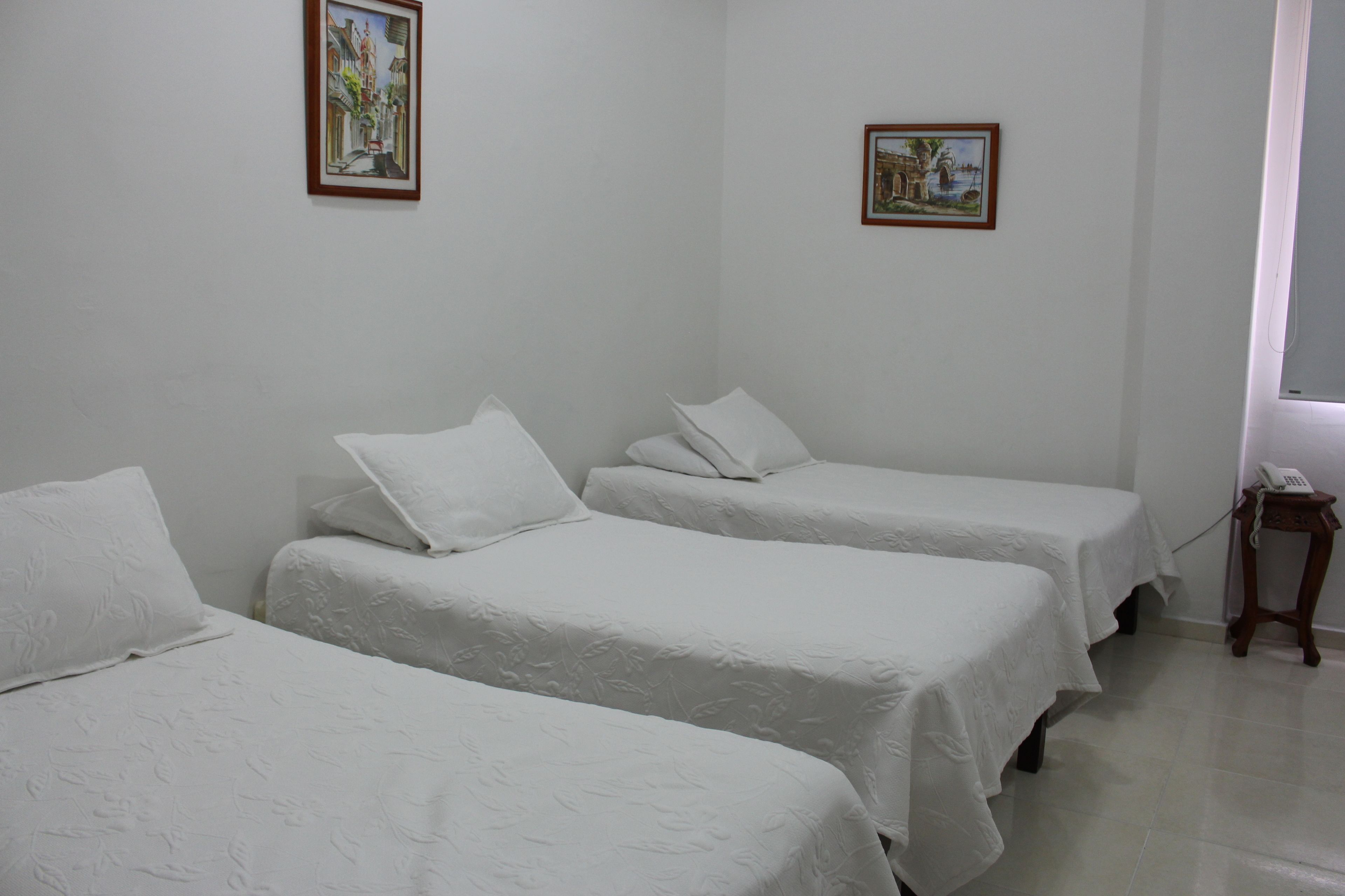 A room with three single beds, white bedding, and two framed pictures on the walls.