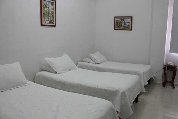 Una habitación con tres camas individuales, ropa de cama blanca y dos cuadros en las paredes.