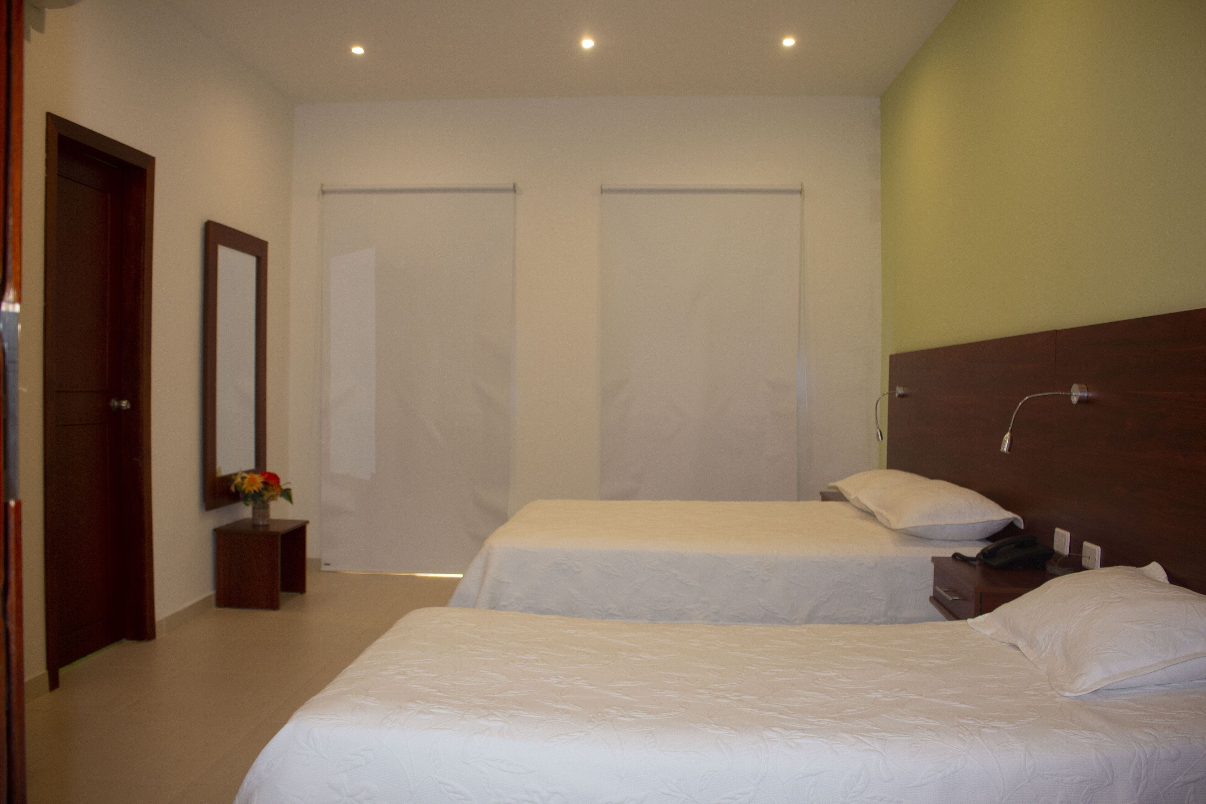 Habitación de hotel con dos camas, cabecero de madera, mesita de noche con teléfono y espejo en la pared.