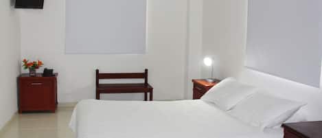 A neatly arranged bedroom with a bed, a wooden bench, a nightstand with a lamp, and a small table with a vase of flowers.