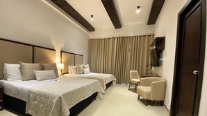Habitación de hotel con dos camas, un escritorio, una silla y un televisor en la pared.