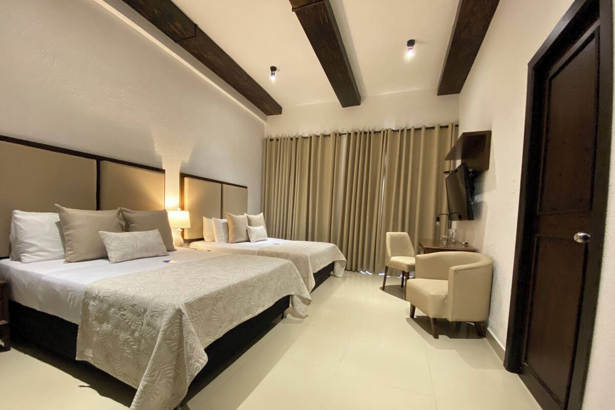 A hotel room with two beds, a desk, a chair, and a TV on the wall.