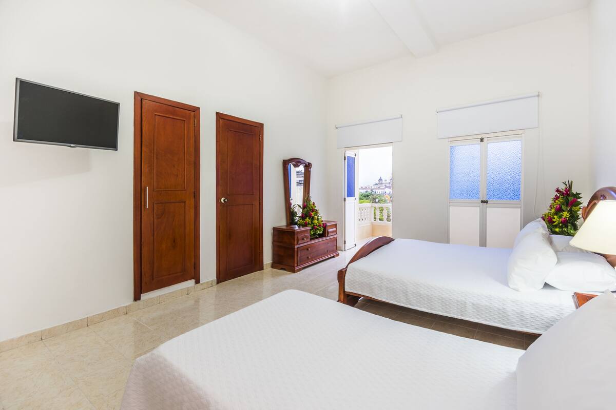 A hotel room with two beds, a TV, wooden doors, a dresser with a mirror, and a view of the sea through a window.