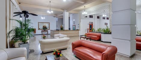A spacious lobby with a reception desk, seating area with sofas, and potted plants.
